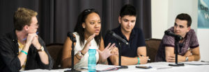 Vote Everywhere Alumni Association, 4 panelists sitting at a table in front of microphones. One panelist is speaking.